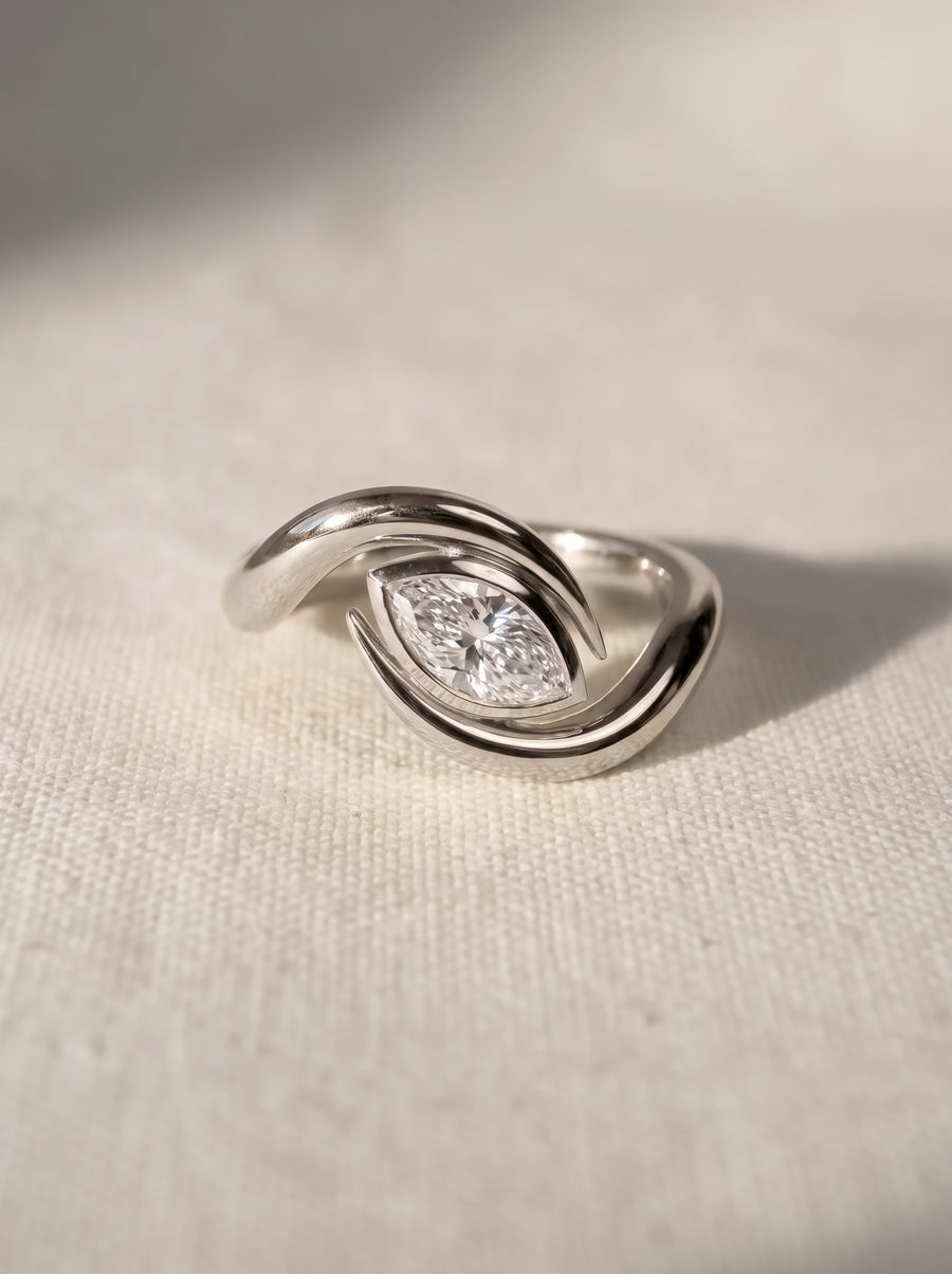 Silver engagement ring featuring a marquise cut diamond set within a curved, bypass-style polished metal band.