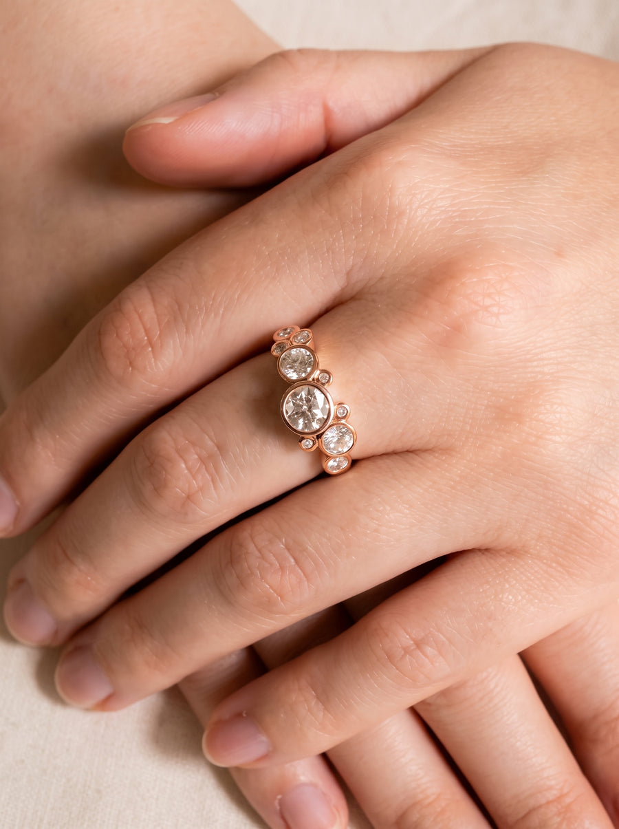 Rose gold ring featuring multiple round cut diamonds in a bubble-style bezel setting worn on a finger.