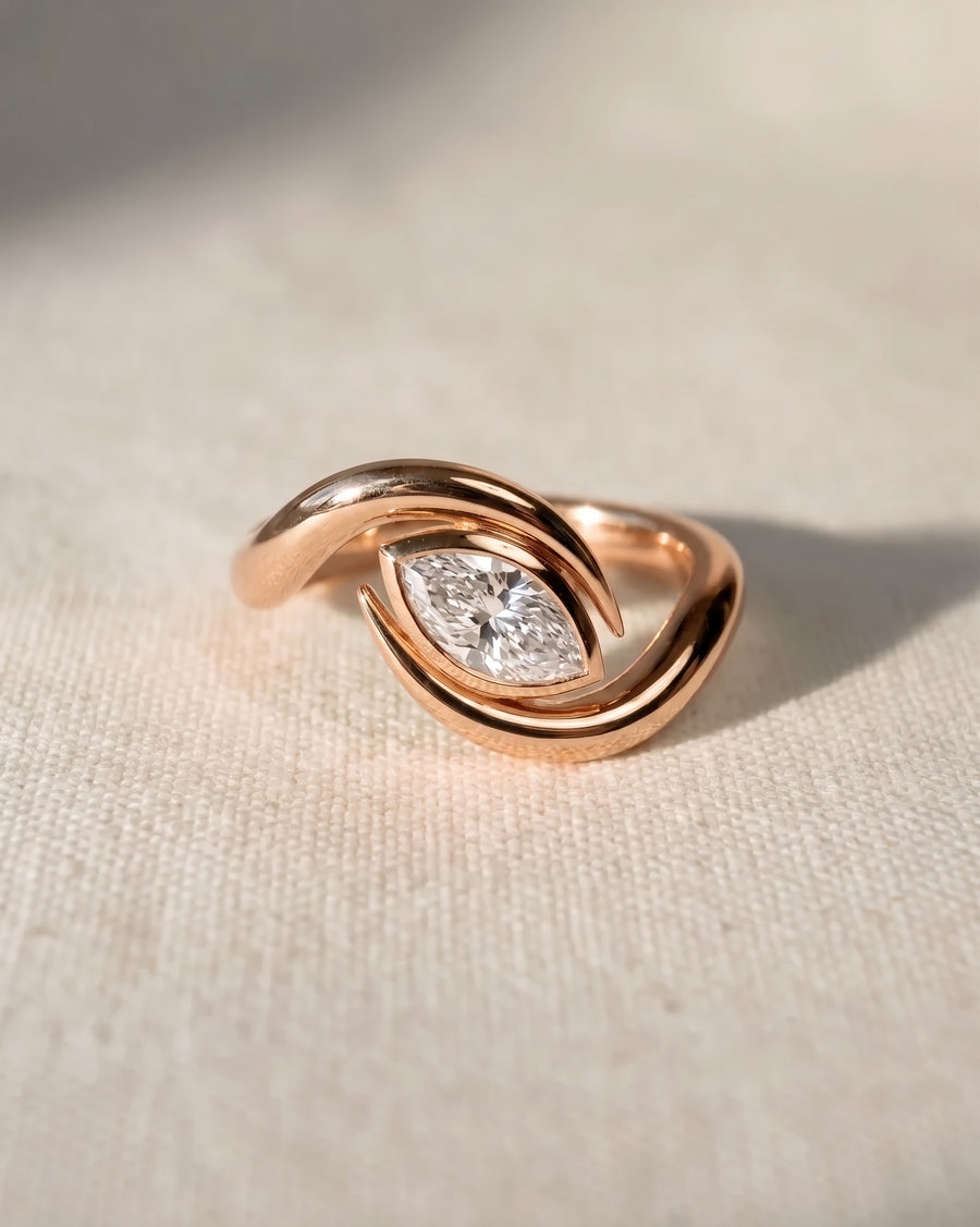 Rose gold engagement ring featuring a marquise cut diamond set in a curved, spiky bypass band.