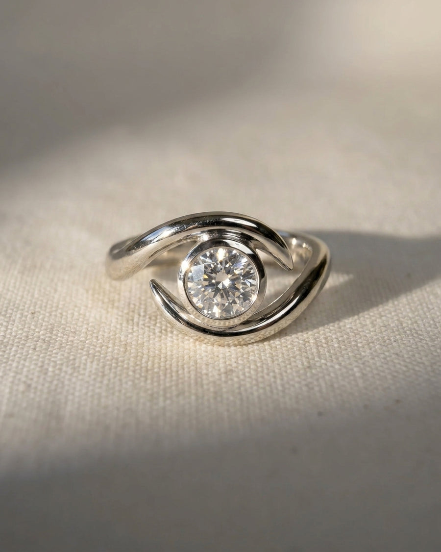 Round cut diamond engagement ring in a platinum spiky bypass setting on a textured fabric background.
