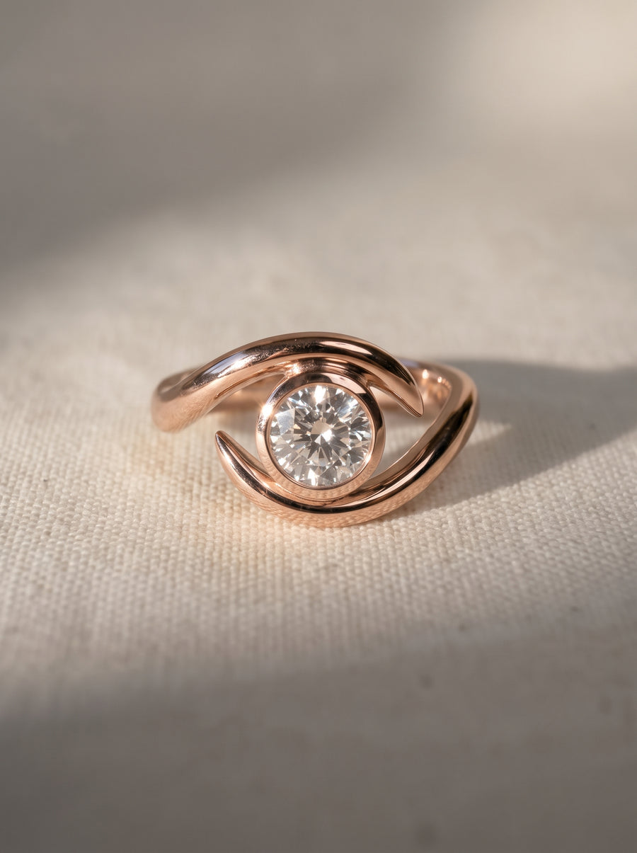 Rose gold engagement ring featuring a round cut diamond in a bezel setting with a curved, spiky band design.