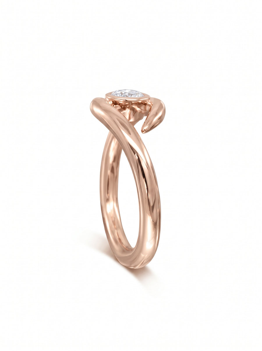 Rose gold engagement ring featuring a round cut diamond in a bezel setting with a spiky, twisted band design.