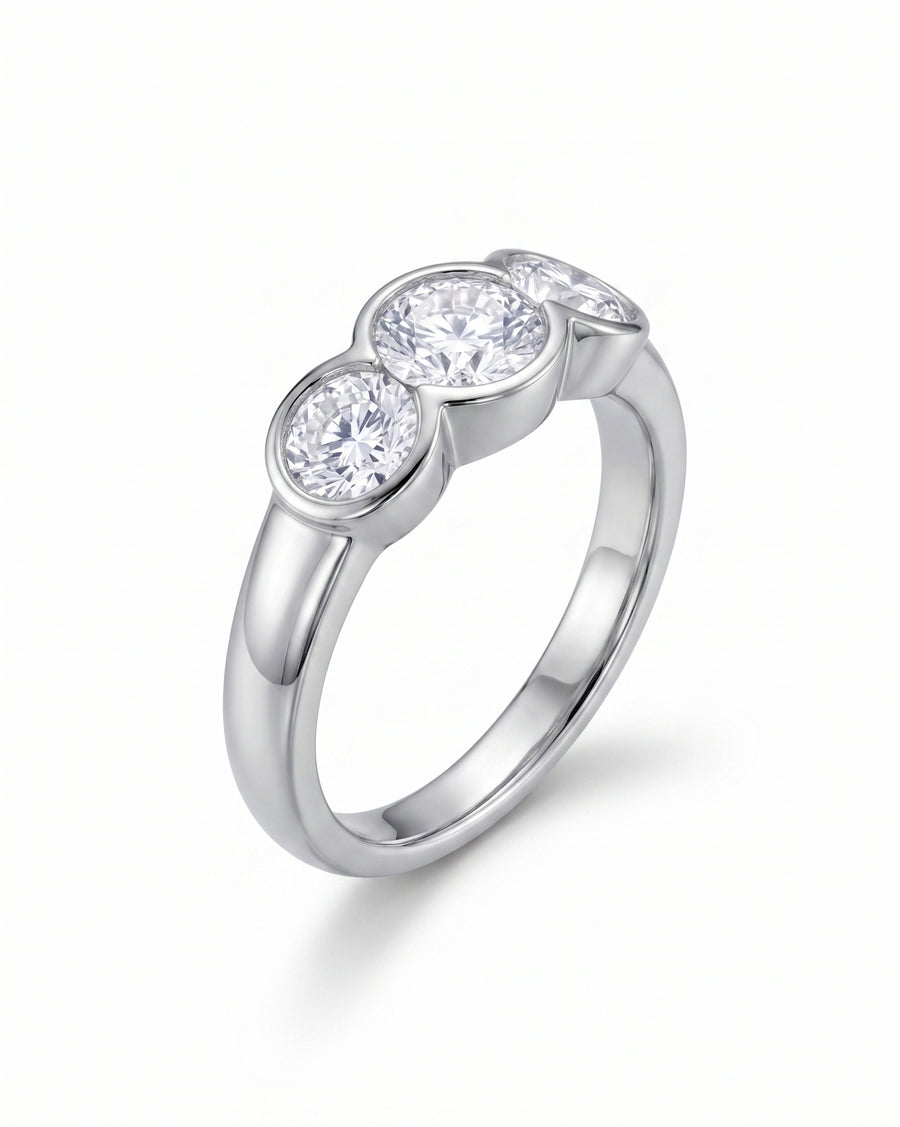 Silver round cut trilogy engagement ring with three bezel-set diamonds.