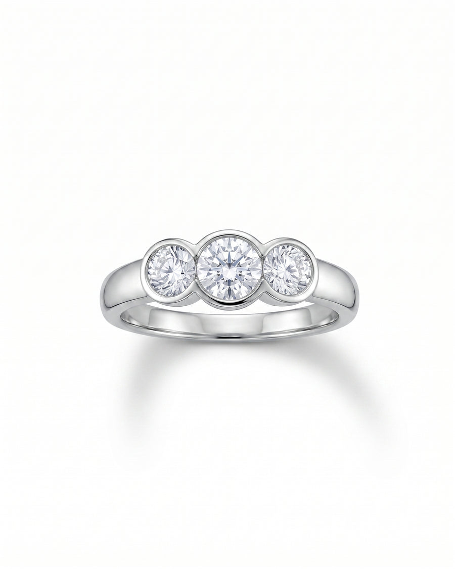 Silver round cut trilogy engagement ring with three bezel-set diamonds.