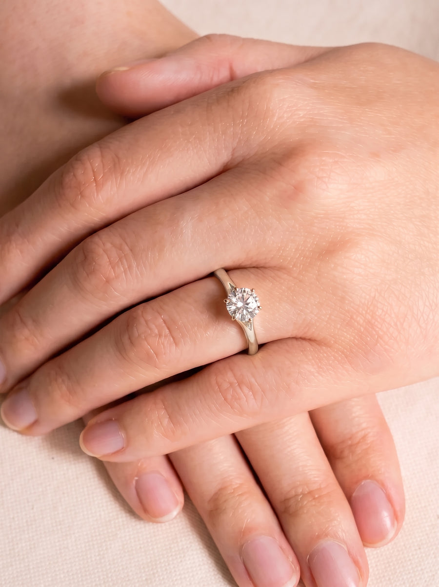 Round cut diamond engagement ring with a gold tulip claw setting worn on a finger.