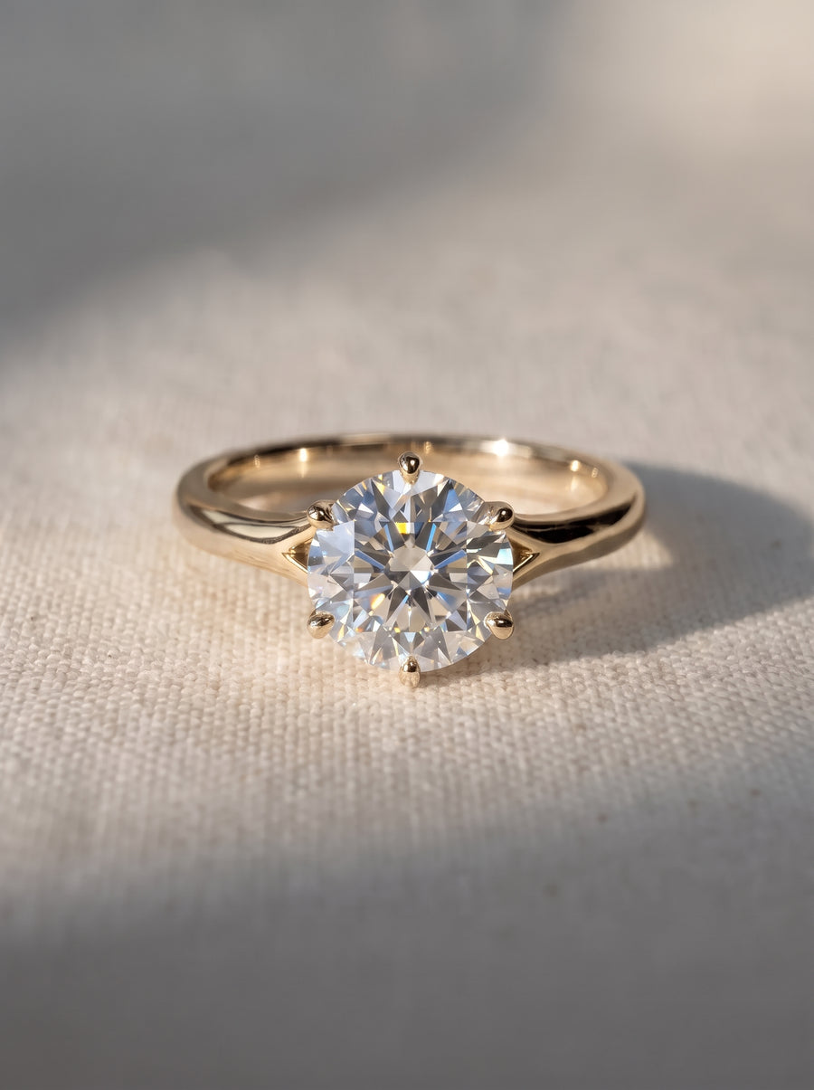 Round cut diamond engagement ring in a gold tulip claw setting on a textured fabric background.
