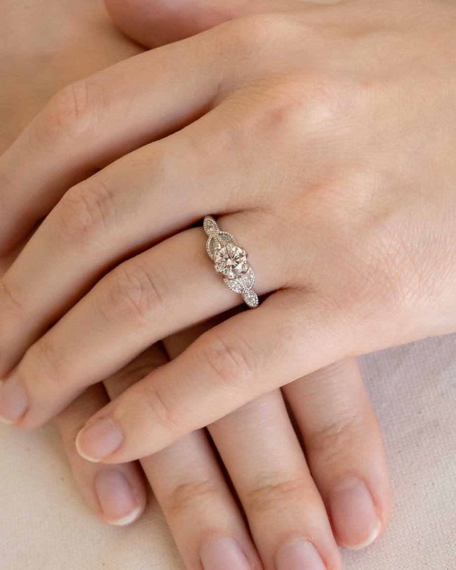 Silver vintage engagement ring with a round cut diamond and pave side stones on a hand.