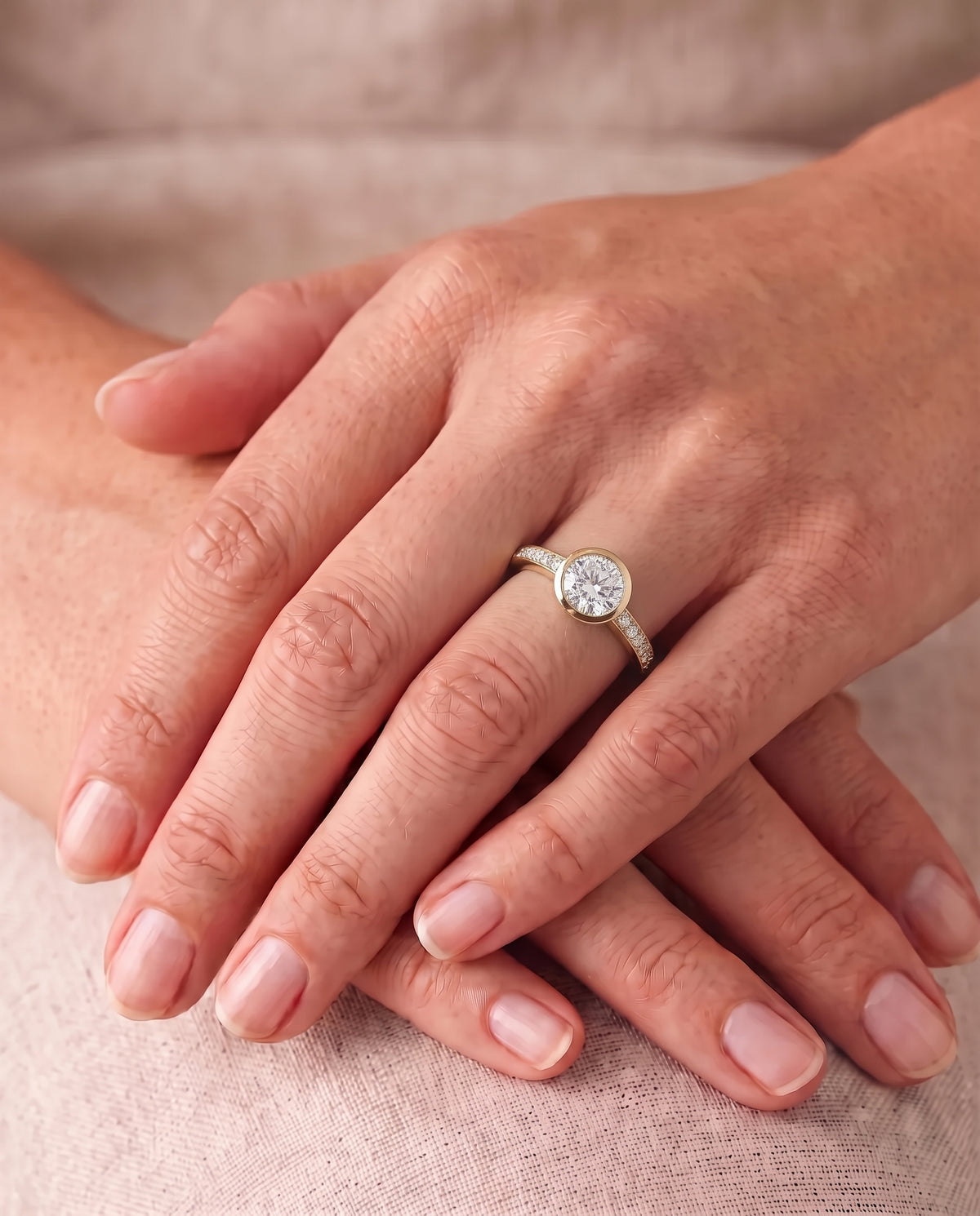 Round diamond engagement ring with a gold bezel setting and pavé diamonds on a yellow gold band.