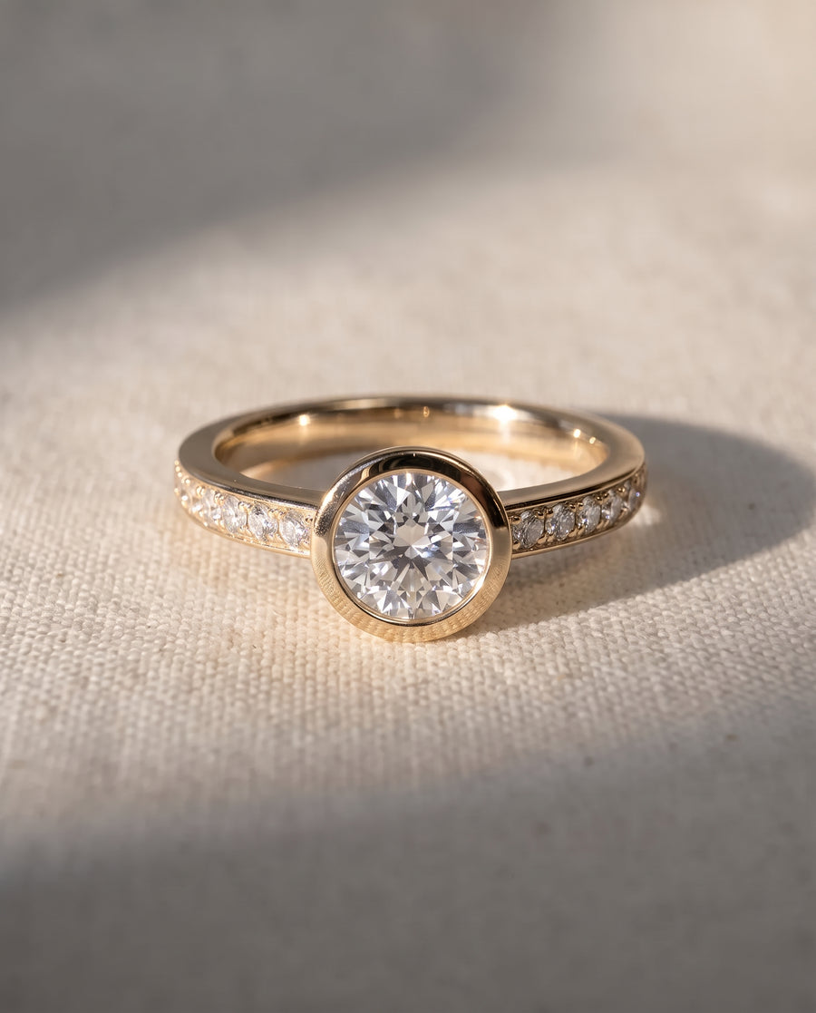9ct yellow gold engagement ring with a round bezel-set diamond and pavé diamond band.