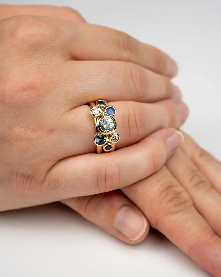 Gold stacking rings with sapphire and aquamarine gemstones on a hand.