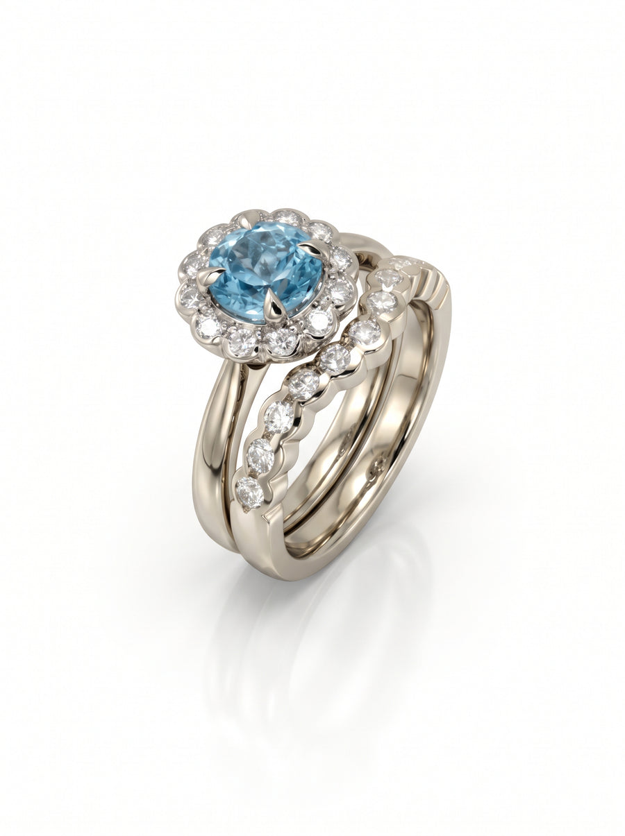 White gold wedding ring set featuring a scalloped band and a blue gemstone halo with diamond accents.