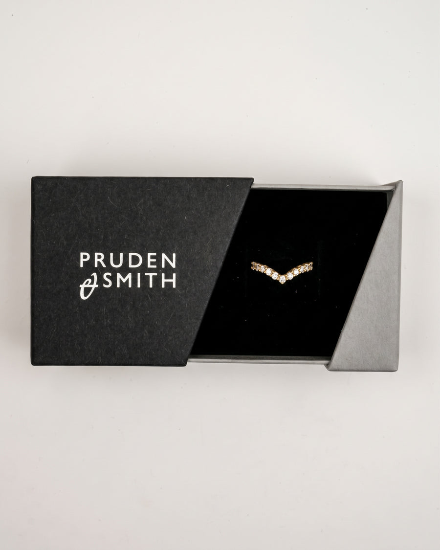 Gold v-shaped wedding band featuring a row of small round diamonds in a black jewelry box.