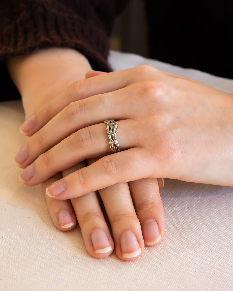Hand wearing a unique, organic-shaped silver wedding ring with natural textures