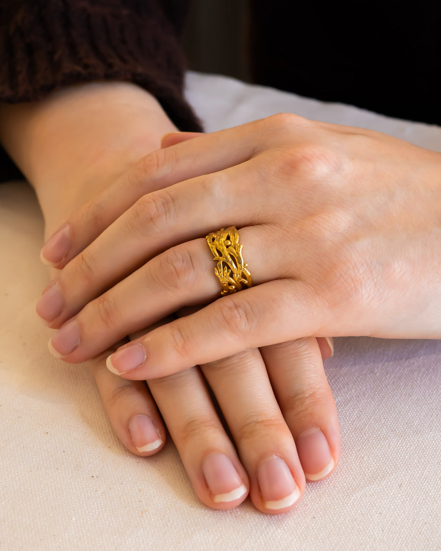 Hand wearing a textured gold wedding ring with organic shapes and intricate detailing