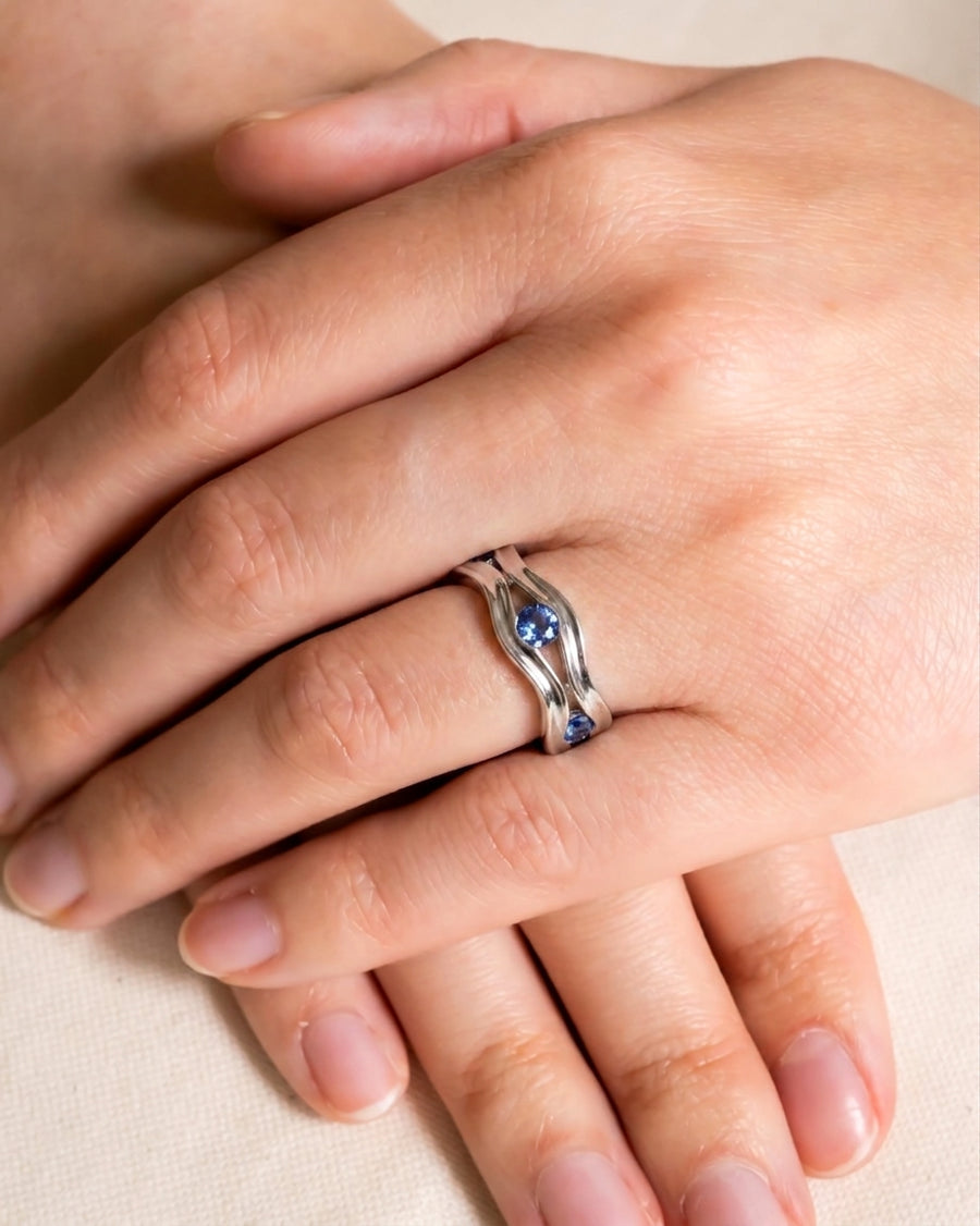 Silver hammered eternity ring with three blue birthstones on a hand.