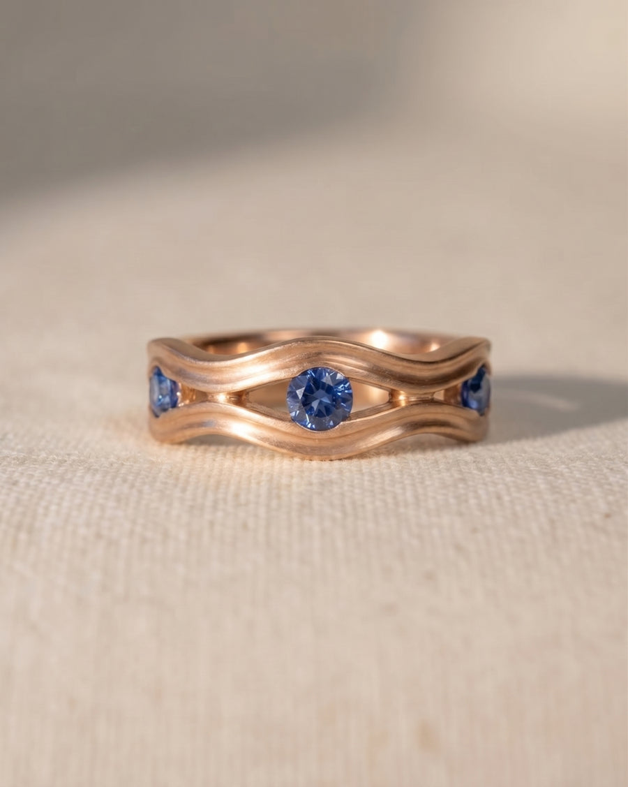 Rose gold eternity ring with wavy hammered design and three blue topaz gemstones.