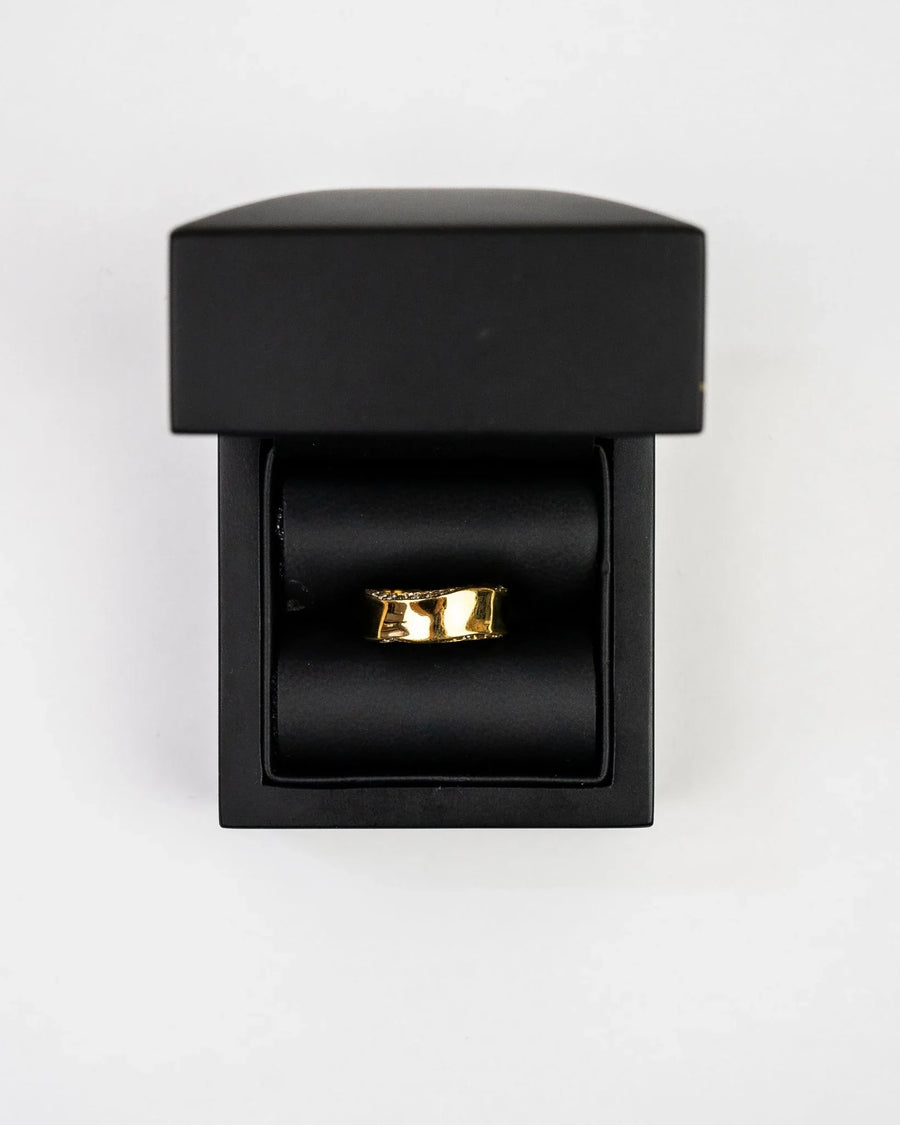Gold eternity ring with side hammered edge and diamonds in a black box.