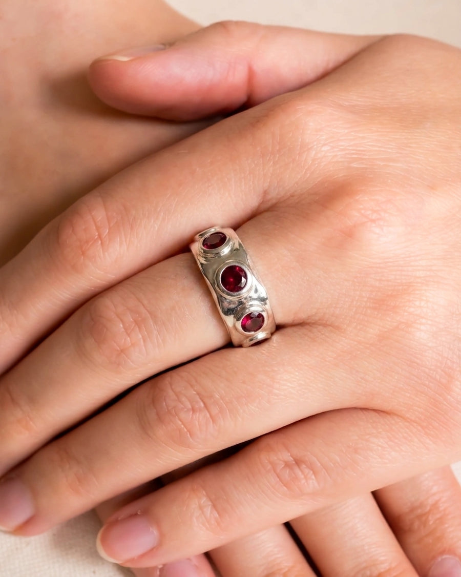 White gold eternity ring with three round rubies and a hammered texture.