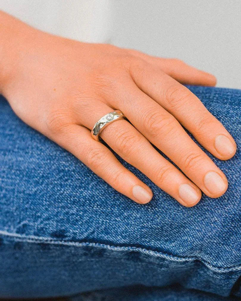 Hand wearing a hammered mixed metal gold diamond ring with organic texture, casual jeans background