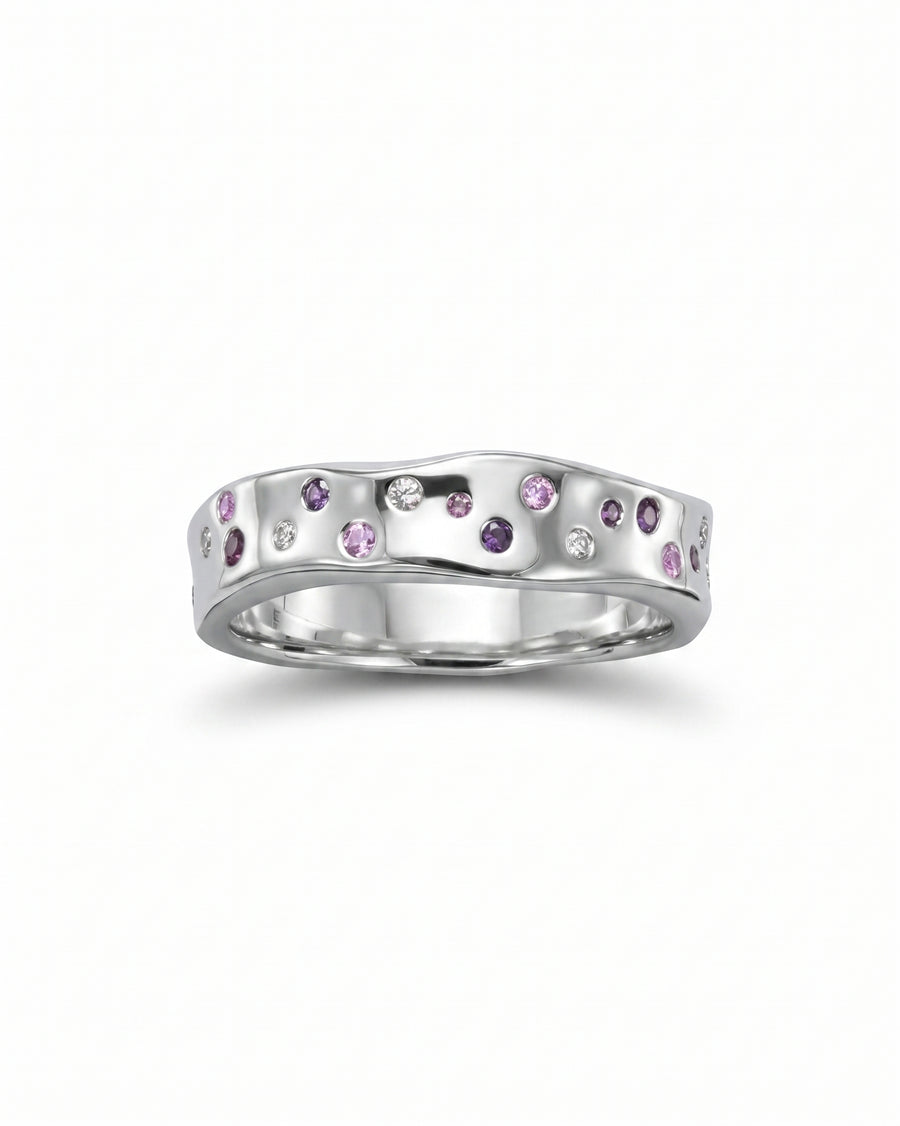 Silver eternity ring with wavy, hammered design and scattered ruby, pink sapphire, and diamond gemstones.