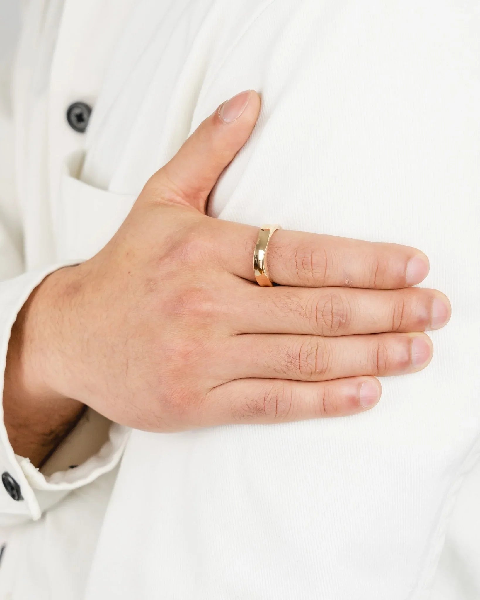 Hand wearing a hammered solid gold wedding ring, close-up, on a white shirt background
