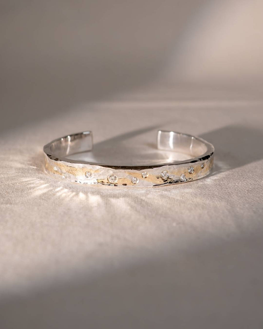 Handmade silver and gold textured cuff bangle with sparkling diamonds on a neutral fabric background