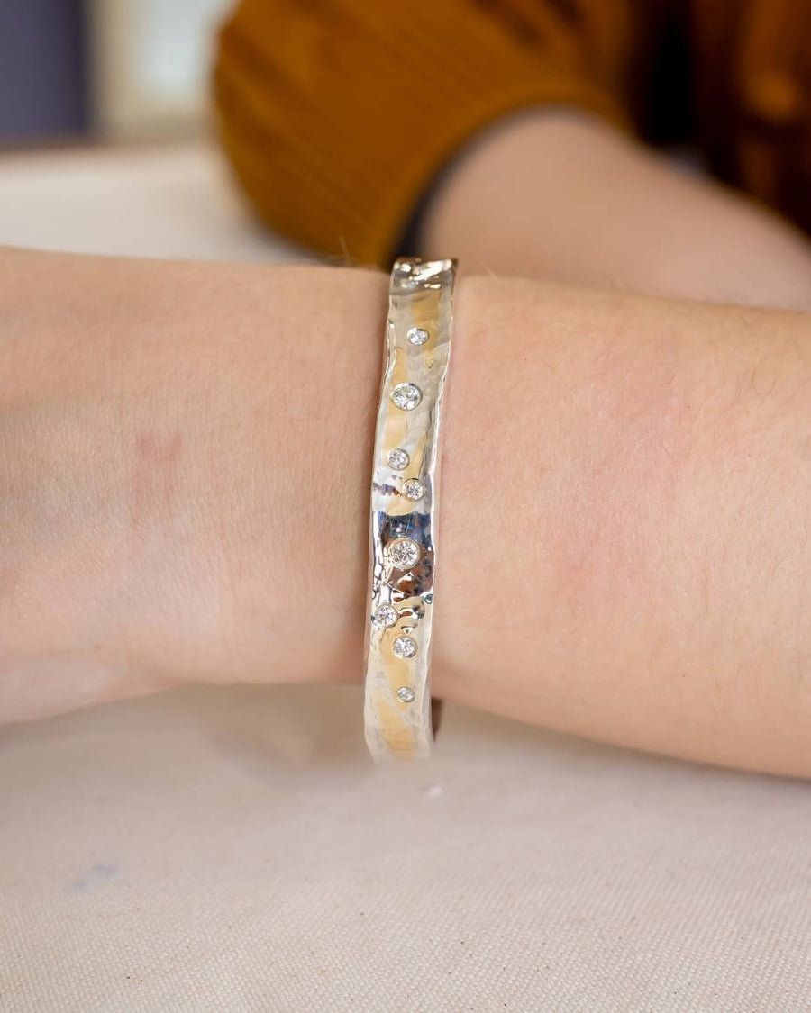 Hand wearing a handmade silver and gold bangle with diamond accents and organic texture