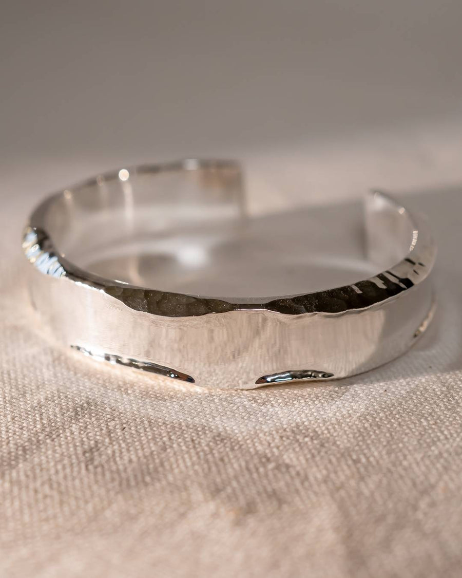 Handmade hammered silver cuff bracelet with organic texture on a neutral fabric background