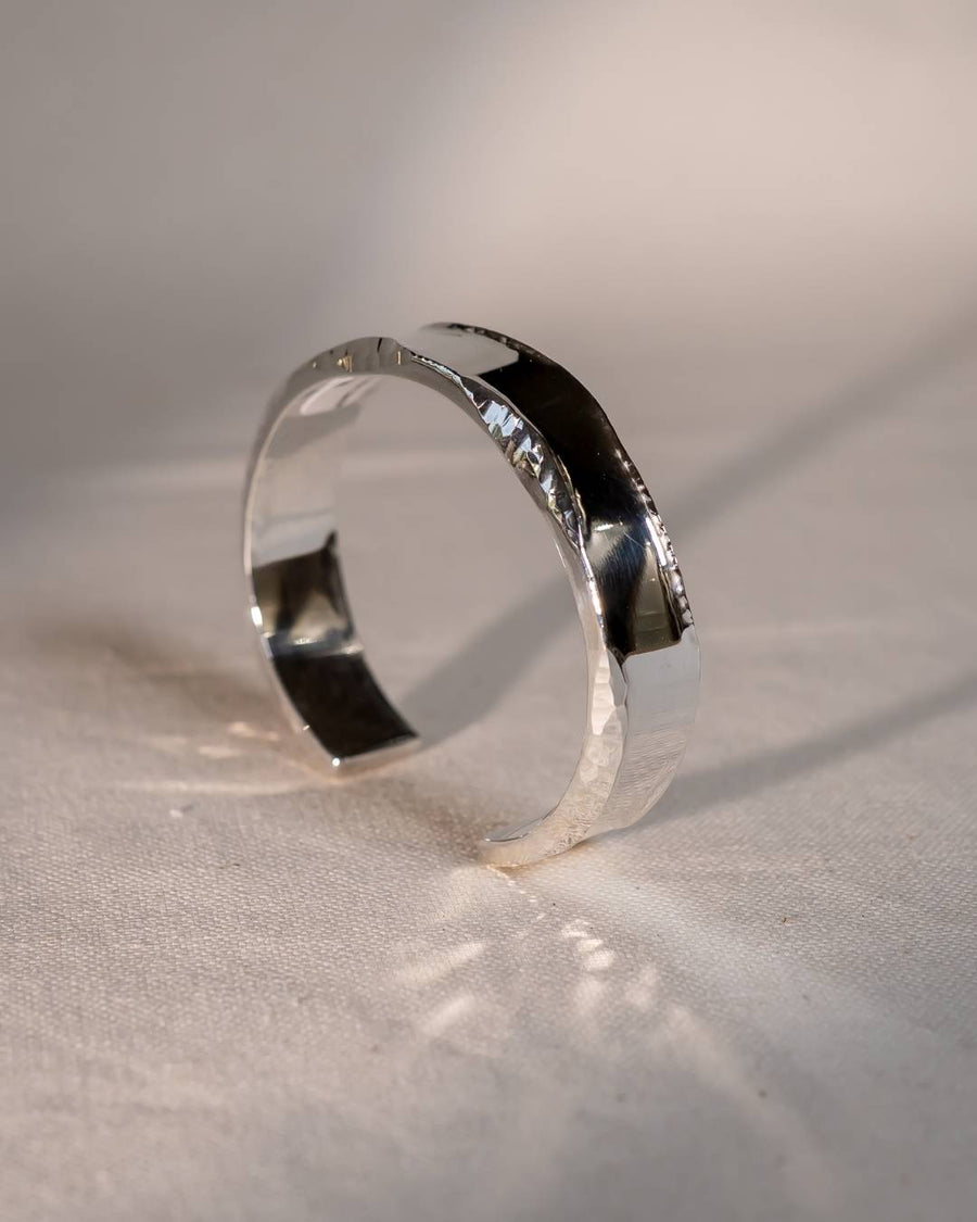 Handmade silver cuff bracelet with organic hammered texture on neutral fabric