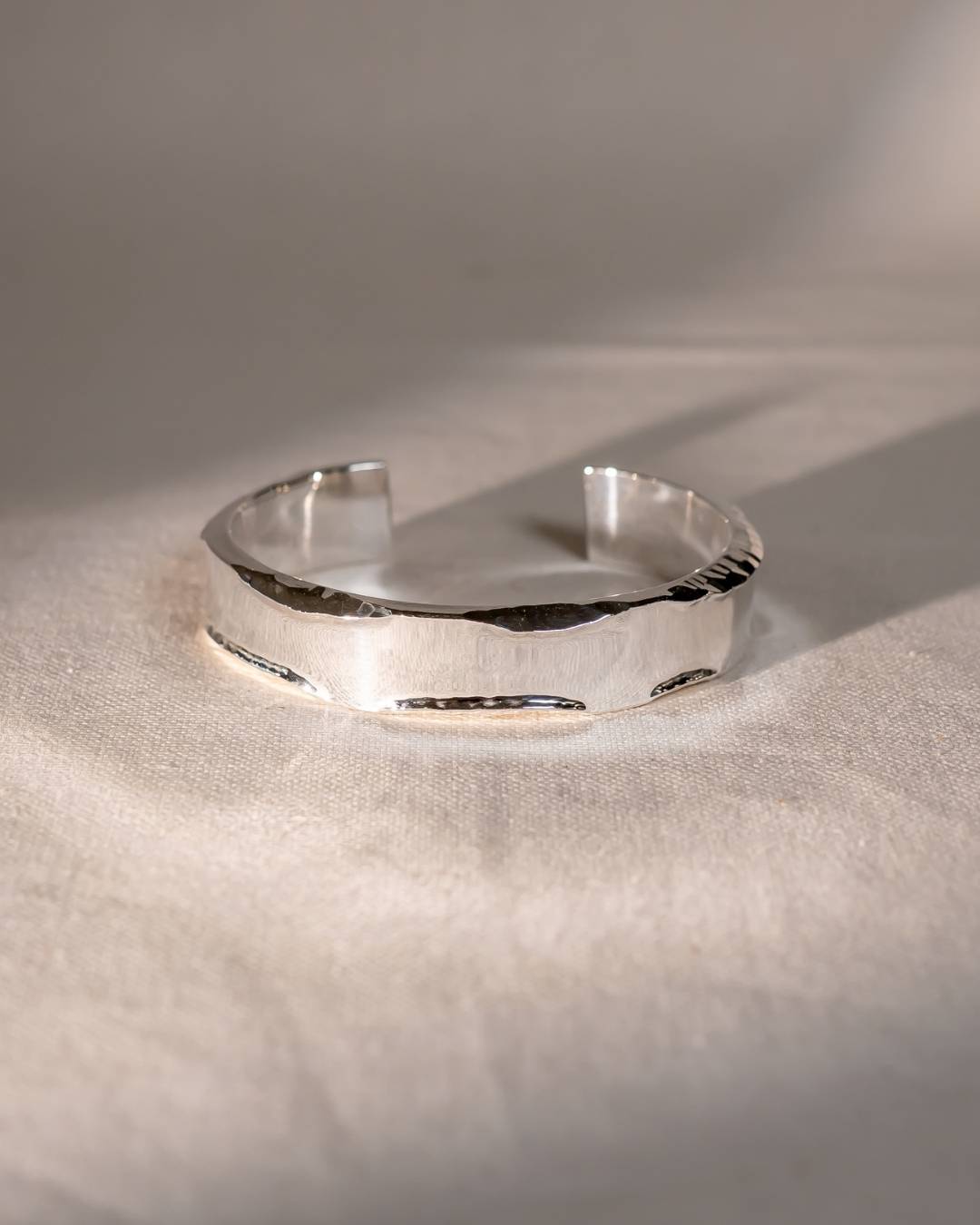 Handcrafted silver cuff bracelet with organic, textured edges on a soft fabric background