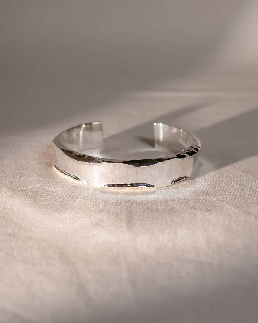 Handcrafted silver cuff bracelet with organic, textured edges on a soft fabric background