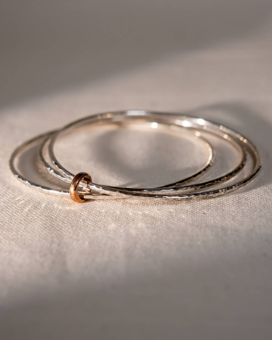 Three handcrafted silver bangles with a single gold ring, textured finish, on fabric