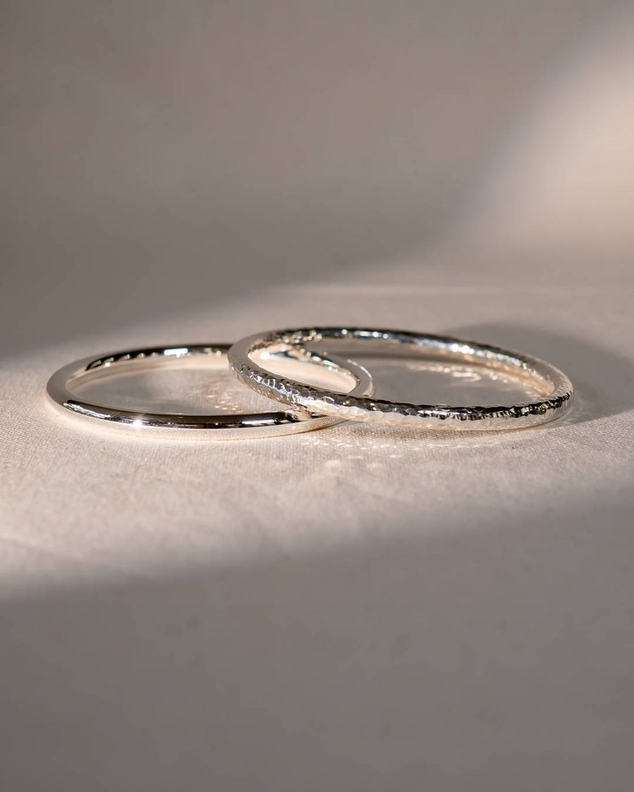Two handcrafted silver rings with smooth and hammered textures on a soft fabric surface