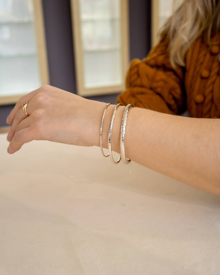 Hand wearing three silver textured bangles and a gold ring, showcasing artisan jewellery