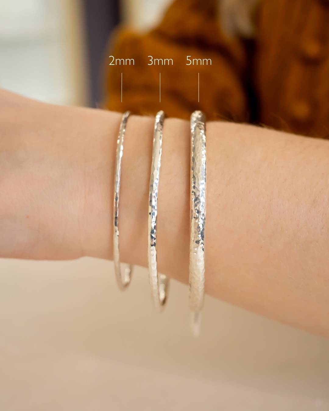 Hand wearing three hammered silver bangles in 2mm, 3mm, and 5mm widths