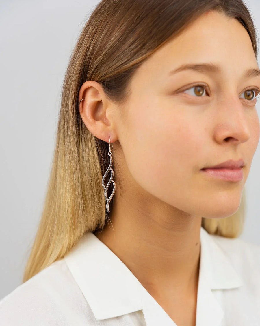 Woman wearing handcrafted silver three-section drop earrings with organic twisted design