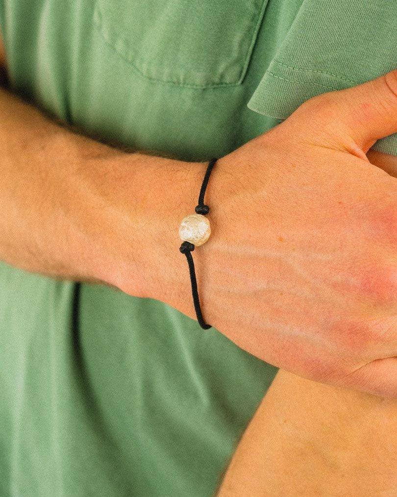 Hand wearing a silver nugget bead on a black faux leather bracelet, natural setting