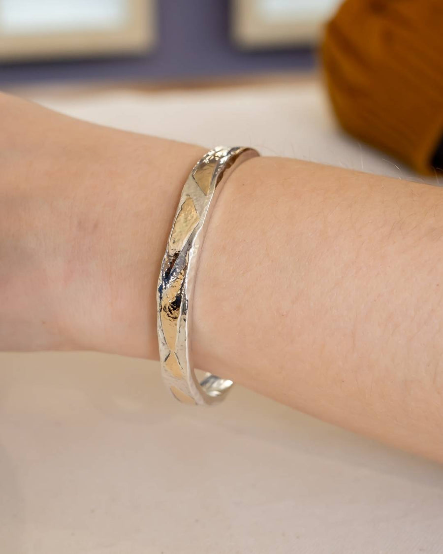 Silver and gold hammered bangle on a wrist.