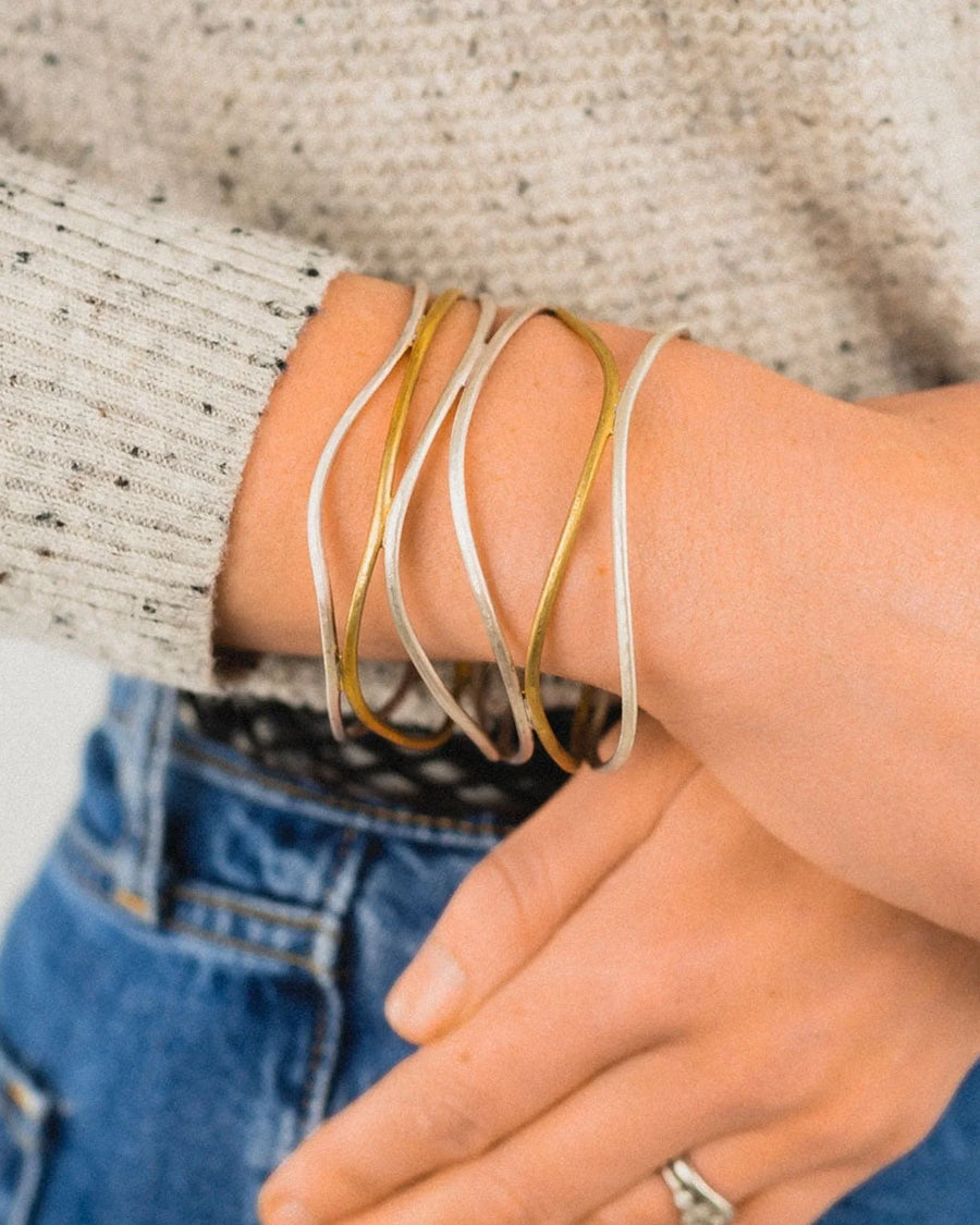 Hand wearing a six-strand solid silver and gold cuff bangle, casual jeans and sweater