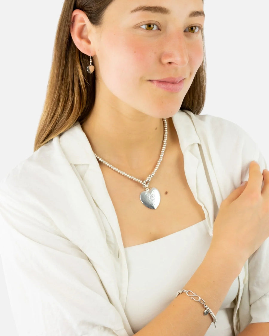 Woman wearing a silver nugget necklace with a hammered heart pendant, matching bracelet and earrings