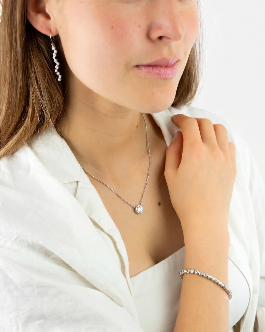 Silver chain necklace with a round bezel-set diamond pendant worn by a woman.