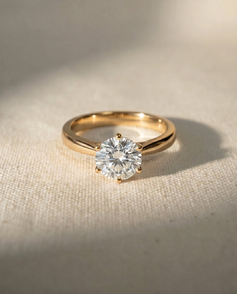 Gold engagement ring with a round diamond in a six-claw setting.