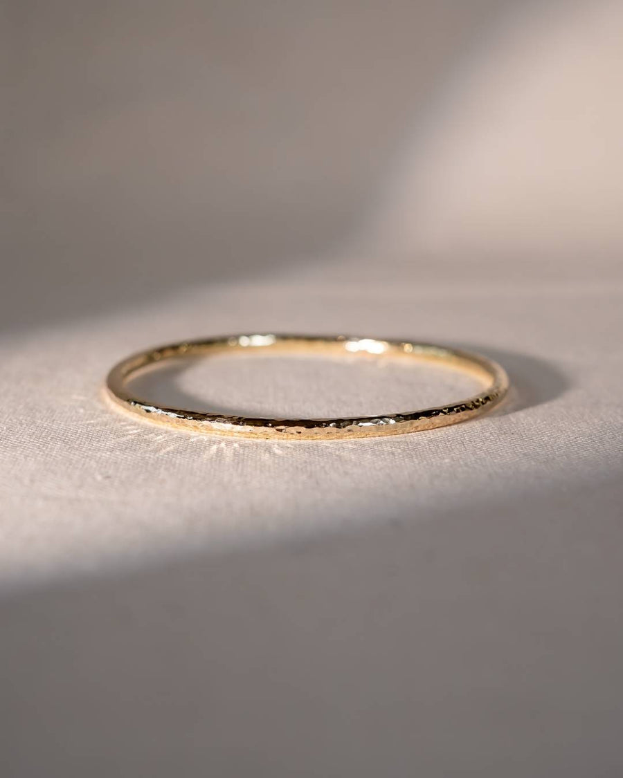 Delicate handmade gold ring with textured finish on a light fabric background