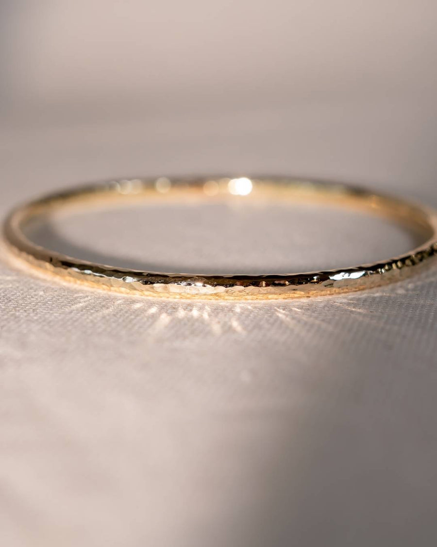 Textured gold bangle with organic handmade finish resting on a soft fabric surface