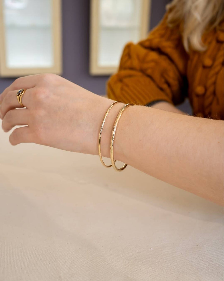 Woman wearing two textured gold bangles and a gold ring, showcasing artisan handmade jewelry