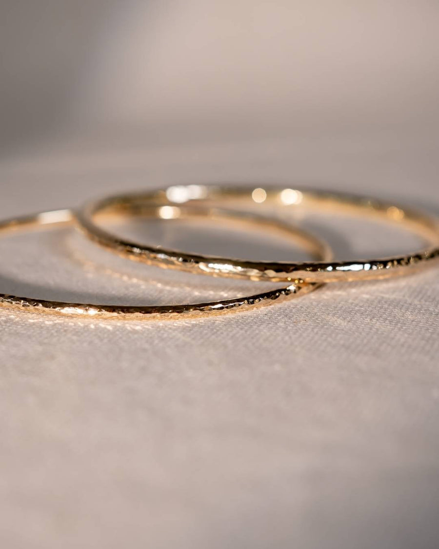 Close-up of handmade gold bangles with a hammered, organic texture on a soft fabric surface