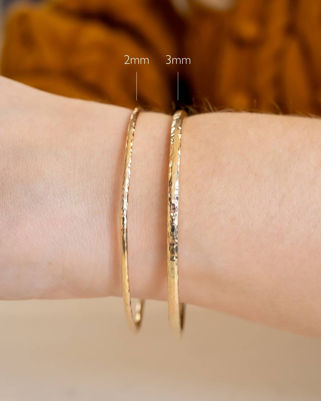 Two hammered gold bangles, 2mm and 3mm wide, worn on a wrist for size comparison