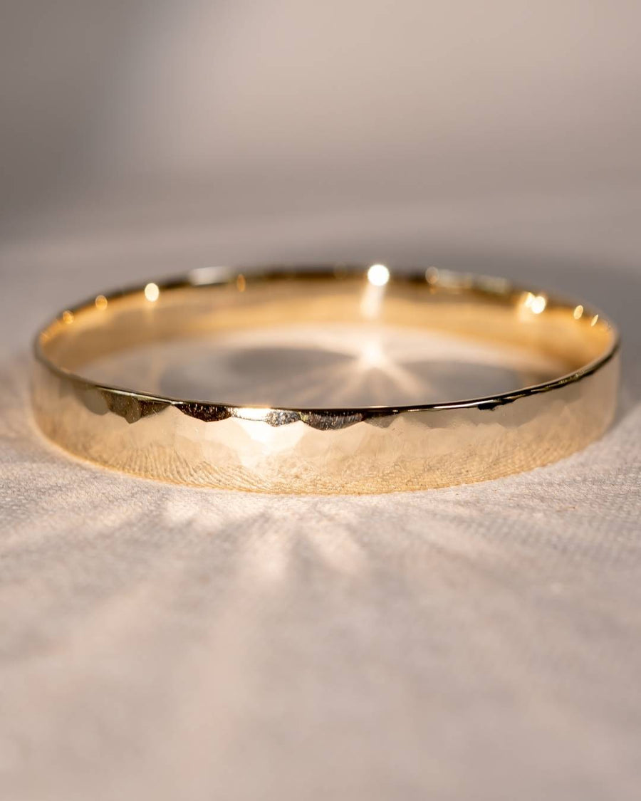 Handcrafted hammered gold bangle with organic texture on a soft fabric background