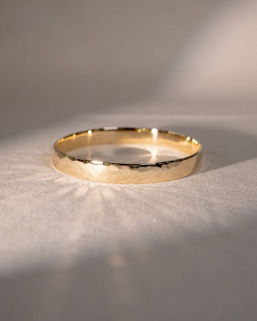 Handcrafted gold bangle with organic hammered texture on a soft neutral fabric