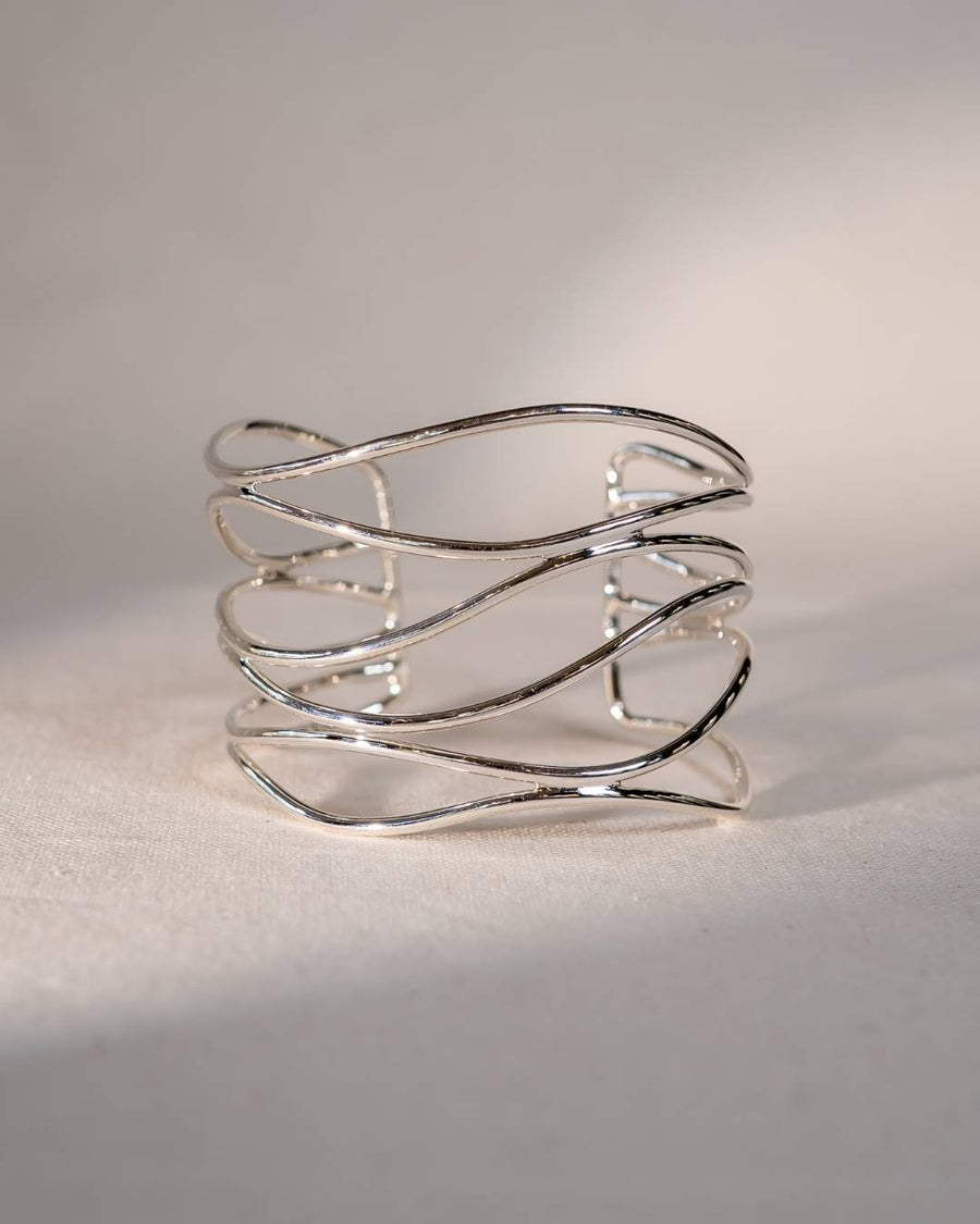 Handmade silver cuff bracelet with organic, wavy lines on a neutral fabric background